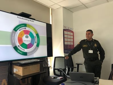 In the picture to the left, Captain Escalante is presenting on the Peacebuilding Model used by the National Police of Colombia. In the picture to the right, Kroc School students are walking on the floor made from the firearms handed over by the FARC as part of the peace process.
